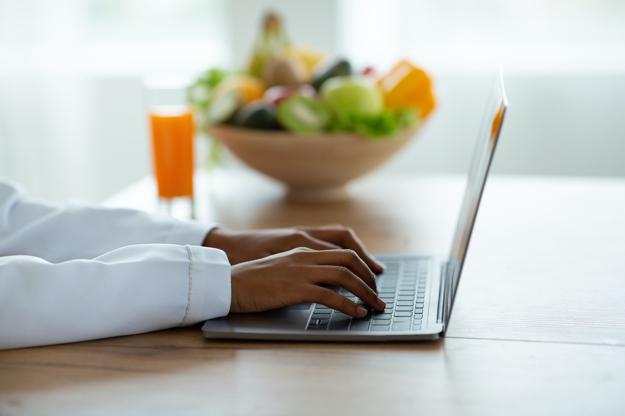 Cropped view of black female dietitian with laptop consulting patient online at clinic, free space